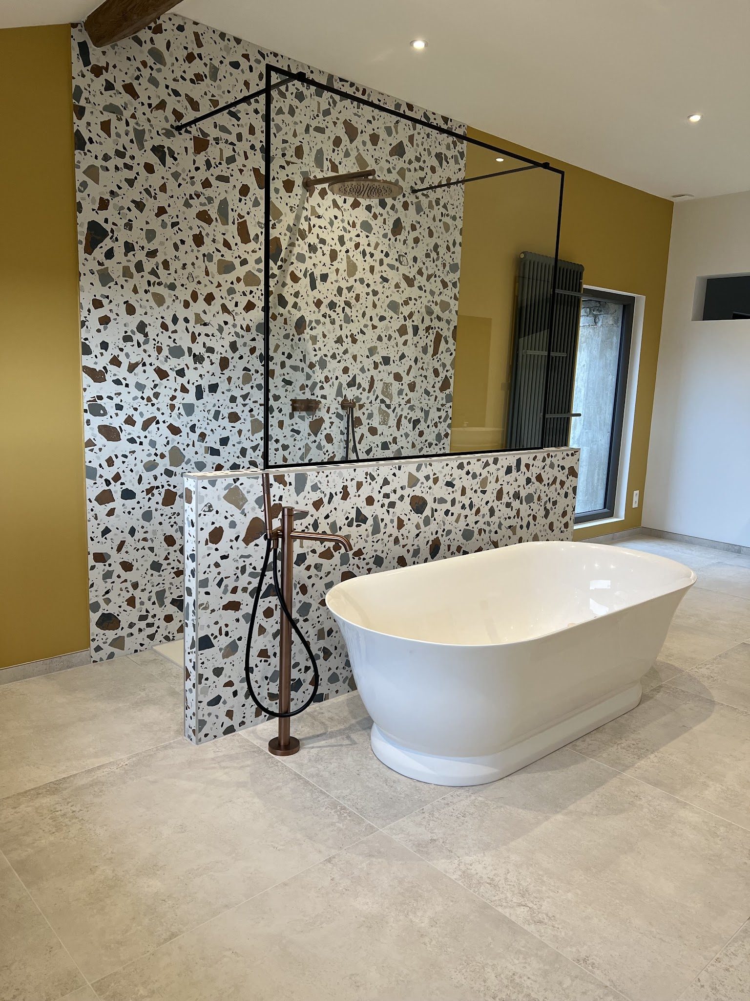 Salle de bains avec mur en terrazzo, douche ouverte et baignoire îlot